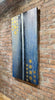 Centered-left-brick-wall-mixed-media-wood-art-artist-Cie-Hoover-Abstract art piece with blue and gold patterns on a brick wall