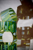 Lighthouse-glass-artist-Evan-Seeling-A sculptural glass vase made of stacked, wavy translucent green glass sections with a central cutout.