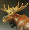 Macho-Man-detail-bronze-sculptor-Jeremy-Bradshaw-A close-up of a moose sculpture or figurine in side profile, showing large antlers, a dark face and neck, and a textured brown and orange body.